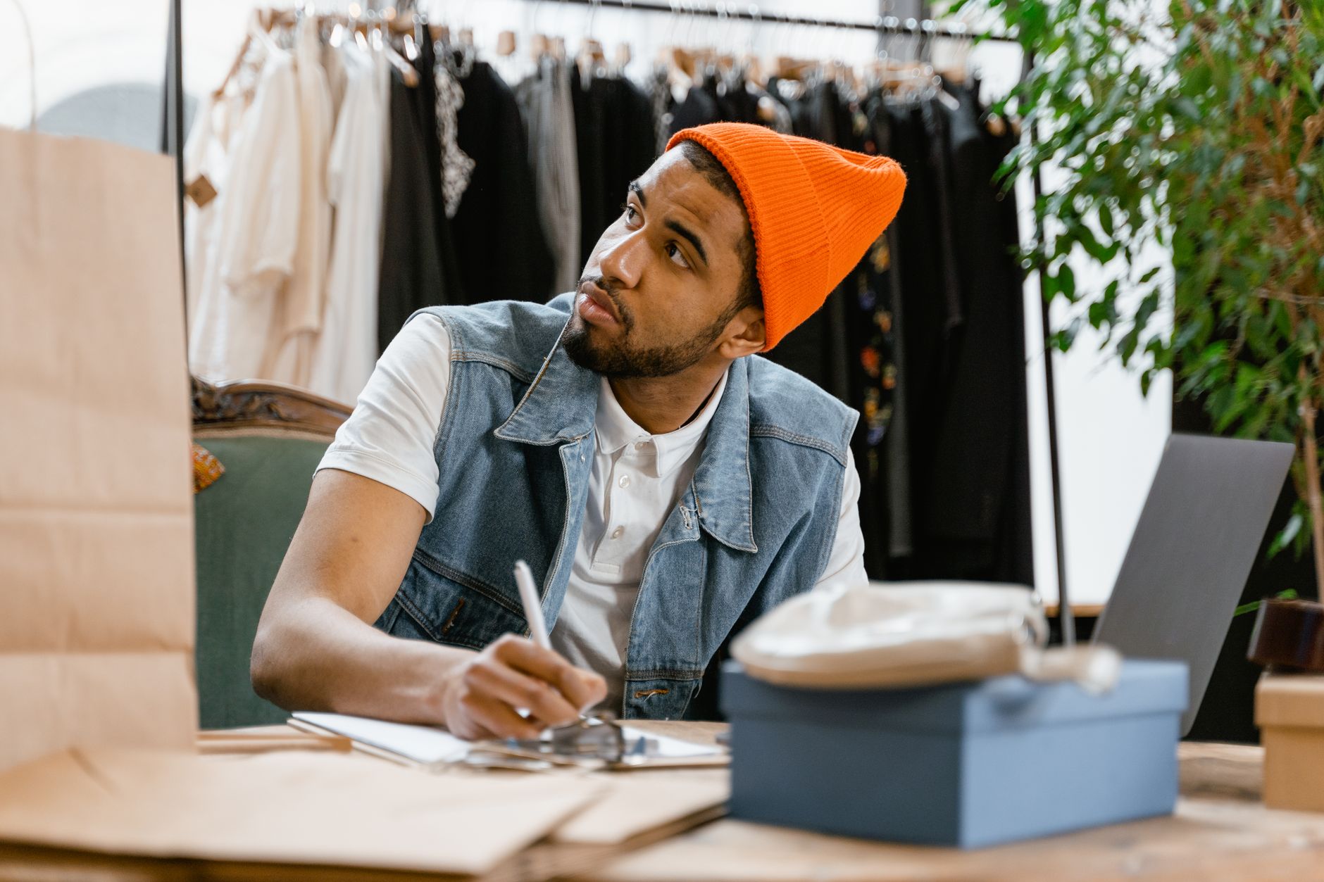 Homme avec un bonnet coloré écrivant à une table dans une boutique de vêtements.